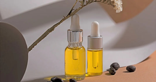 Deux flacons d’huile de jojoba visage pure avec pipette, posés sur fond naturel, entourés de graines de jojoba et d’une fleur séchée